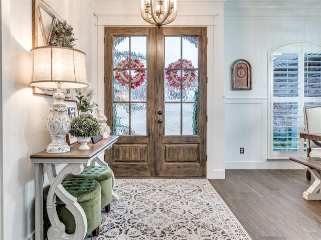 foyer entrance featuring wood-type flooring, crown molding, a chandelier, and french doors