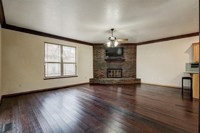 unfurnished living room with dark wood-type flooring, ceiling fan, crown molding, and a brick fireplace