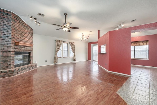 unfurnished living room featuring lofted ceiling, wood-type flooring, ceiling fan with notable chandelier, and a brick fireplace