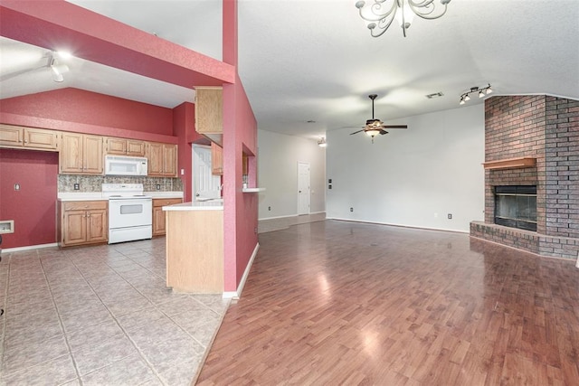 kitchen with white appliances, ceiling fan, a brick fireplace, decorative backsplash, and vaulted ceiling