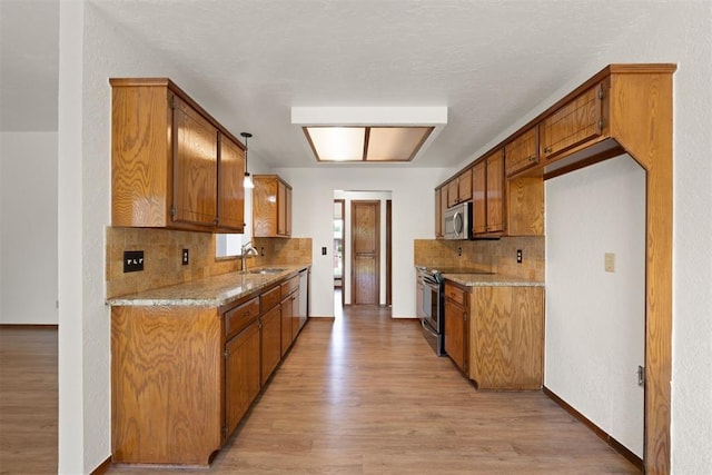 kitchen featuring stainless steel appliances, light stone countertops, pendant lighting, and light wood-type flooring