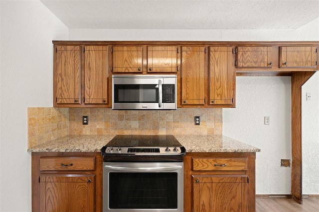 kitchen with tasteful backsplash, light stone countertops, light hardwood / wood-style flooring, and stainless steel appliances