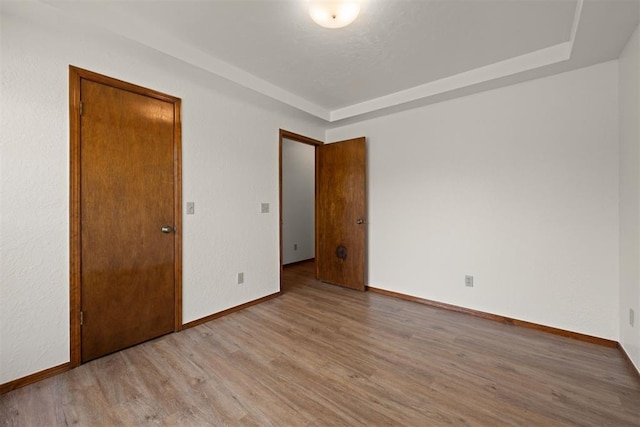 unfurnished bedroom with a raised ceiling and light wood-type flooring