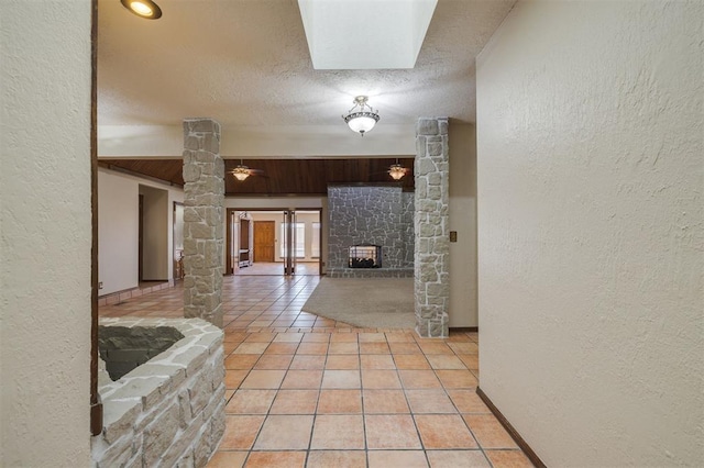 corridor with light tile patterned floors, decorative columns, and a textured ceiling