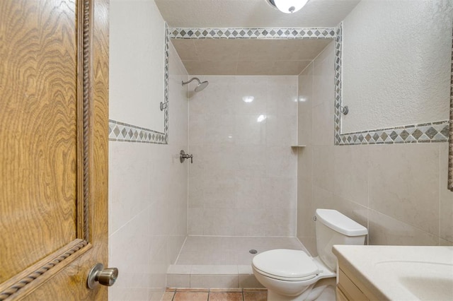 bathroom with vanity, tile walls, toilet, and a tile shower