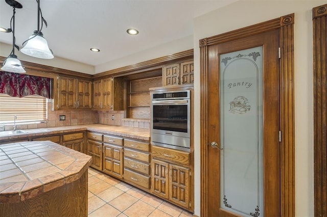 kitchen with tile counters, decorative backsplash, light tile patterned flooring, decorative light fixtures, and stainless steel oven