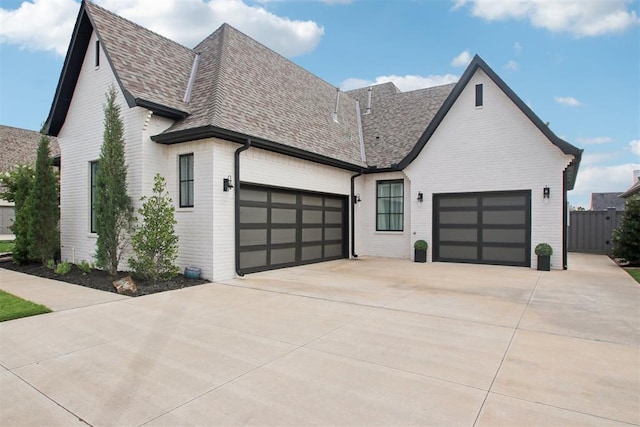 view of front of property featuring brick siding, fence, concrete driveway, roof with shingles, and an attached garage