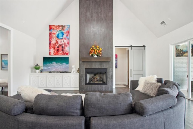 living room with a barn door, wood finished floors, visible vents, and a large fireplace