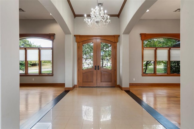 foyer entrance with crown molding, an inviting chandelier, french doors, and light tile patterned floors