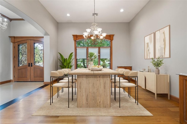 dining area with a wealth of natural light, a notable chandelier, light wood-type flooring, and french doors