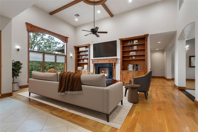 living room with beam ceiling, a towering ceiling, ceiling fan, and light wood-type flooring