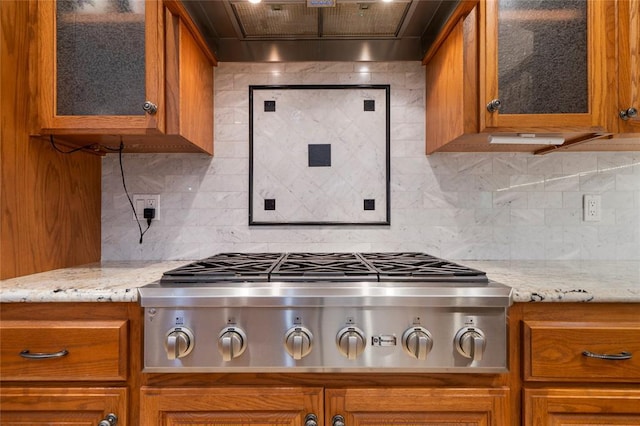 kitchen with light stone counters, decorative backsplash, custom exhaust hood, and stainless steel gas stovetop