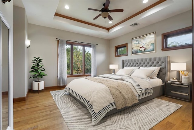 bedroom featuring crown molding, a tray ceiling, ceiling fan, and light wood-type flooring