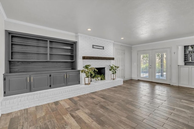 unfurnished living room featuring french doors, crown molding, built in features, hardwood / wood-style flooring, and a fireplace