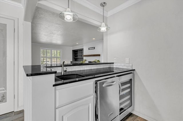 kitchen with sink, hanging light fixtures, wine cooler, ornamental molding, and white cabinets