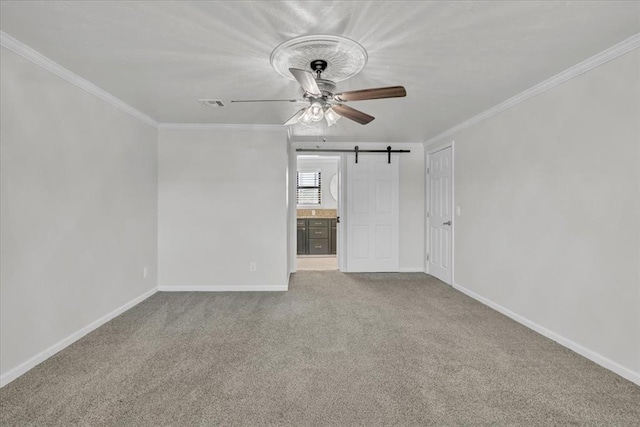 empty room with ornamental molding, a barn door, carpet floors, and ceiling fan