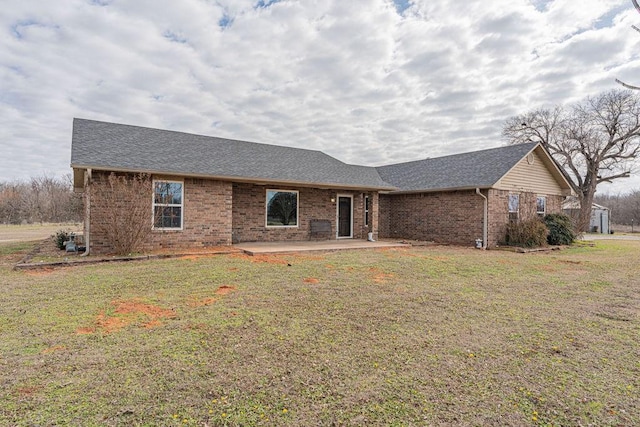 ranch-style house featuring brick siding, roof with shingles, a patio area, and a front yard