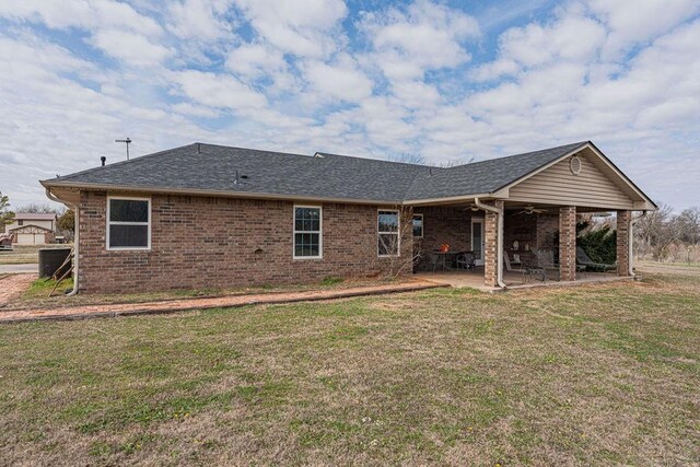 rear view of house featuring brick siding, a yard, roof with shingles, a ceiling fan, and a patio area