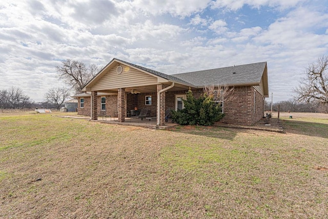 view of front of property with a patio, brick siding, a shingled roof, a ceiling fan, and a front lawn