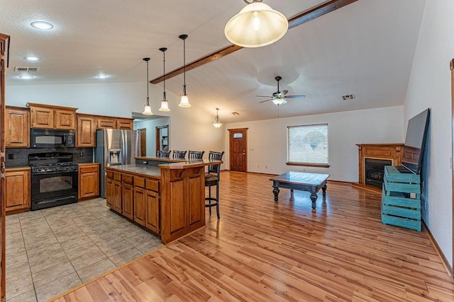 kitchen with visible vents, open floor plan, a kitchen island, black appliances, and a kitchen bar