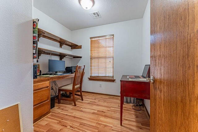 office space with light wood-style floors, visible vents, a textured ceiling, and baseboards