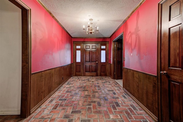 entryway with crown molding, a chandelier, a textured ceiling, and wood walls