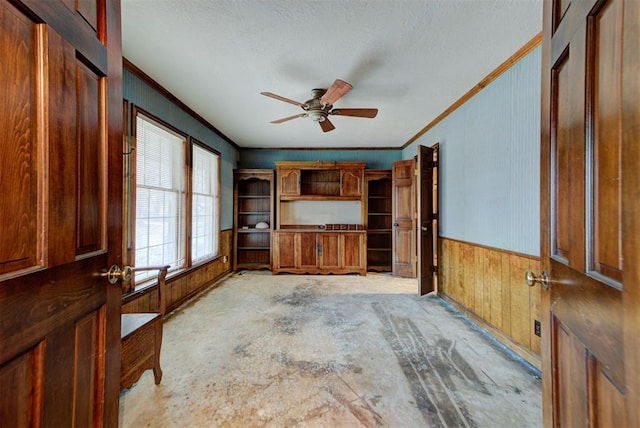 unfurnished living room featuring crown molding, ceiling fan, and wood walls