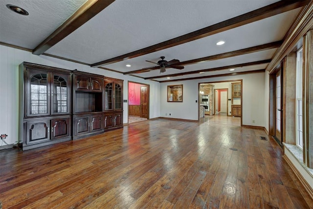 unfurnished living room featuring dark hardwood / wood-style flooring, ceiling fan, beam ceiling, and a textured ceiling