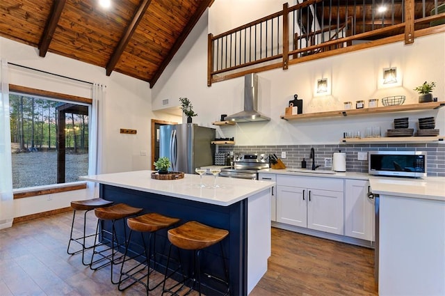 kitchen with wall chimney range hood, sink, a breakfast bar, stainless steel appliances, and white cabinets