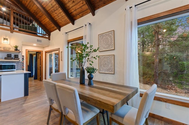 dining area featuring beam ceiling, high vaulted ceiling, light wood-type flooring, and wood ceiling