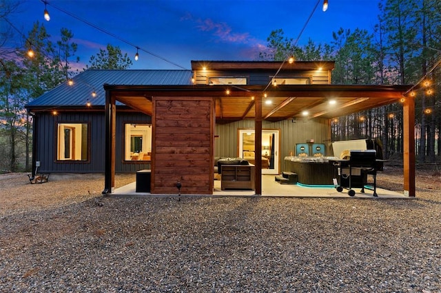 back house at dusk featuring a hot tub and a patio area