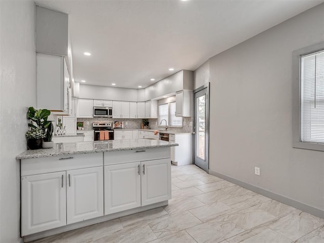 kitchen with white cabinetry, backsplash, light stone counters, kitchen peninsula, and stainless steel appliances