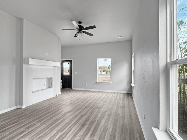 unfurnished living room featuring hardwood / wood-style floors, a fireplace, ceiling fan, and plenty of natural light