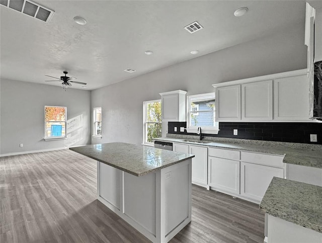 kitchen with light stone counters, sink, a kitchen island, and white cabinets