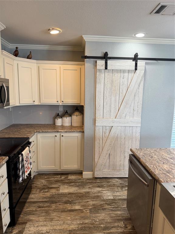 kitchen with a barn door, stainless steel appliances, visible vents, ornamental molding, and white cabinetry