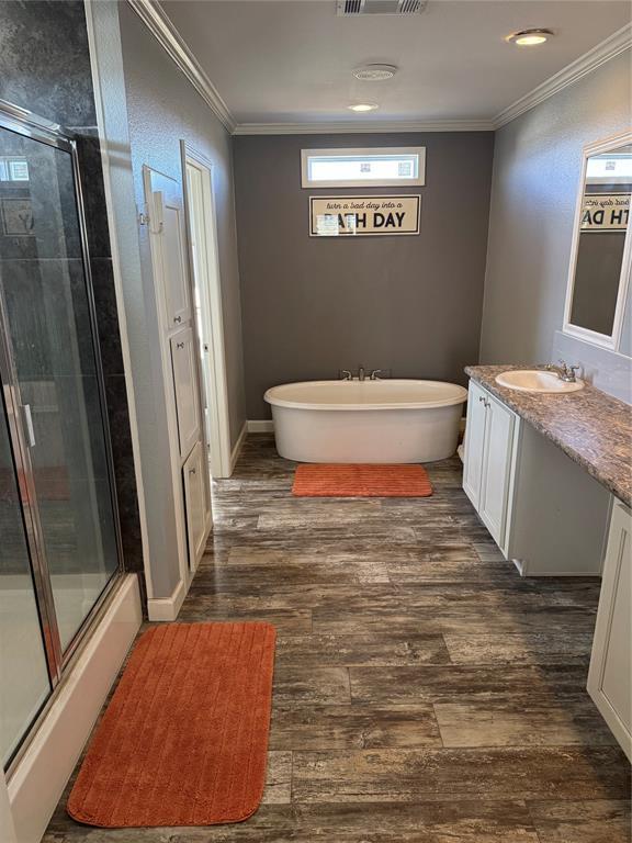 full bathroom with a shower with door, wood finished floors, vanity, ornamental molding, and a soaking tub