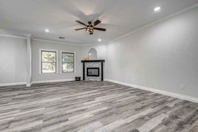 unfurnished living room with ceiling fan, ornamental molding, a stone fireplace, and light wood-type flooring