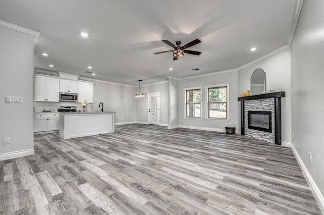 unfurnished living room featuring ornamental molding, a stone fireplace, and ceiling fan with notable chandelier