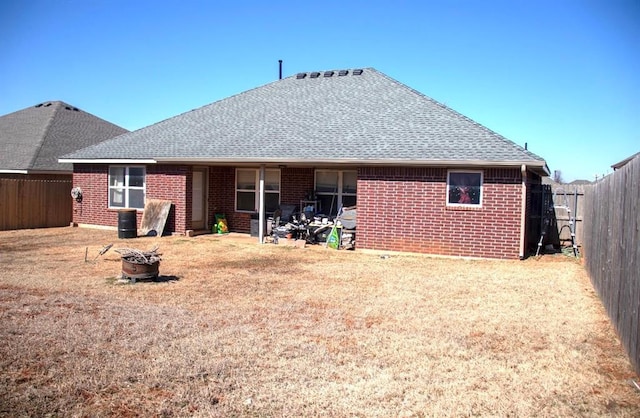 back of house featuring a fenced backyard, an outdoor fire pit, a yard, roof with shingles, and brick siding