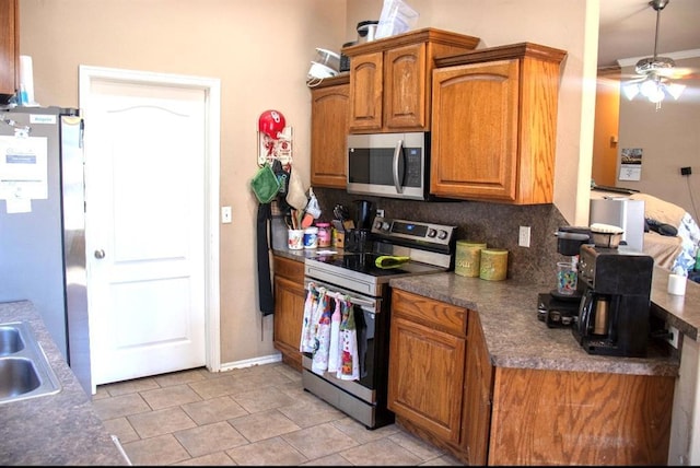 kitchen with a ceiling fan, a sink, tasteful backsplash, appliances with stainless steel finishes, and brown cabinetry