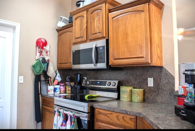 kitchen with backsplash, stainless steel appliances, brown cabinets, and dark countertops