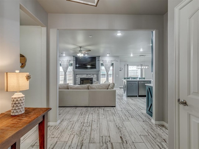 living area with ceiling fan, a fireplace, baseboards, and light wood-style floors