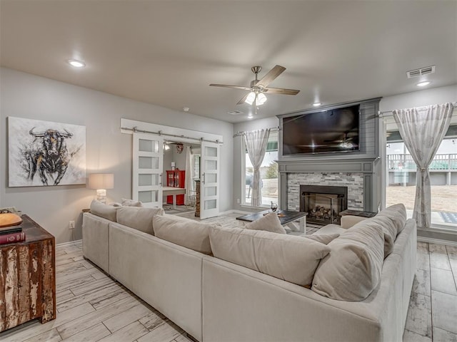 living area with a barn door, baseboards, ceiling fan, light wood-style flooring, and a fireplace