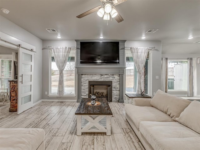 living area with visible vents, a fireplace, light wood-style flooring, and a barn door