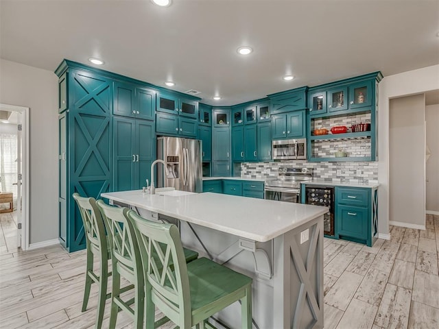 kitchen with wine cooler, a kitchen island with sink, stainless steel appliances, light countertops, and open shelves