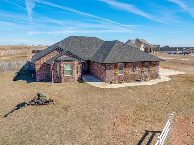 view of front of property with roof with shingles, brick siding, a front lawn, and fence