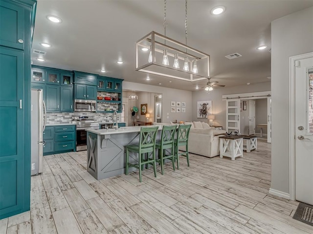 kitchen featuring a center island with sink, light countertops, a barn door, appliances with stainless steel finishes, and open floor plan