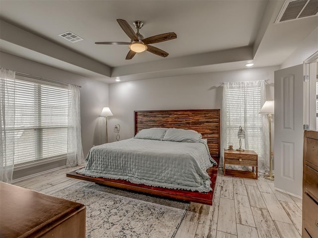 bedroom featuring ceiling fan, light wood-style flooring, visible vents, and a raised ceiling