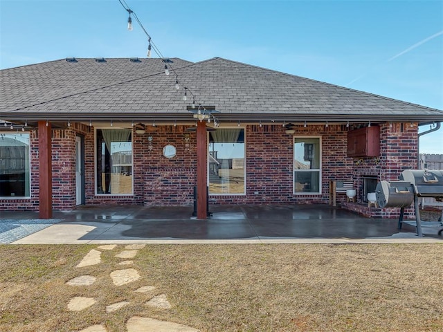 back of house featuring a yard, brick siding, roof with shingles, and a patio area