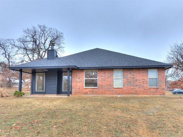 rear view of house with a shingled roof, brick siding, a yard, and a chimney